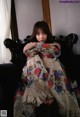 A woman sitting on a black couch in a floral dress.