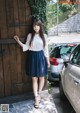 A woman leaning against a wooden door in front of a car.