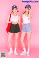 Two young women standing next to each other on a pink background.