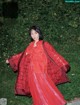 A woman in a red dress standing in front of a bush.