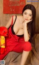 A woman in red overalls sitting on a couch with a teddy bear.