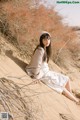 A woman in a white dress sitting on a sand dune.