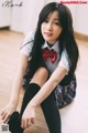 A young woman sitting on the floor wearing a school uniform.