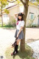 A woman in a school uniform leaning against a tree.