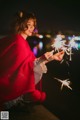 A woman in a red poncho holding sparklers in her hands.